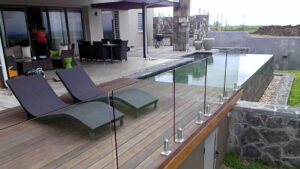 Modern glass railing installation around a sleek outdoor deck, featuring a pool area with lounge chairs and a luxurious patio setup.