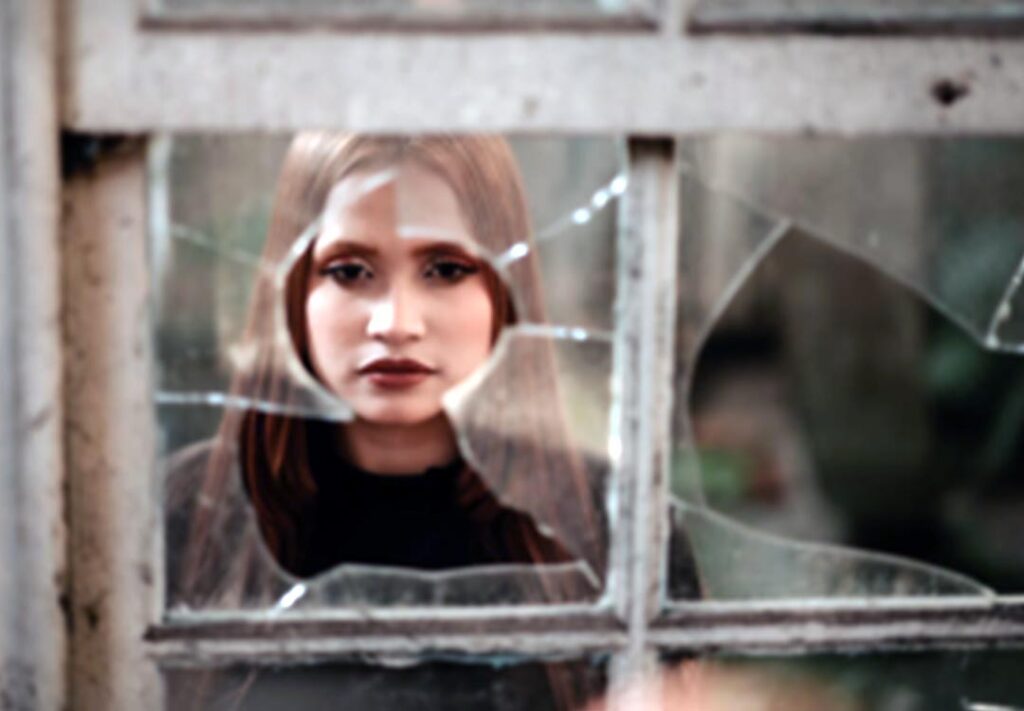Portrait of a woman standing behind a cracked window glass, emphasizing the need for repair or replacement to restore safety and clarity.