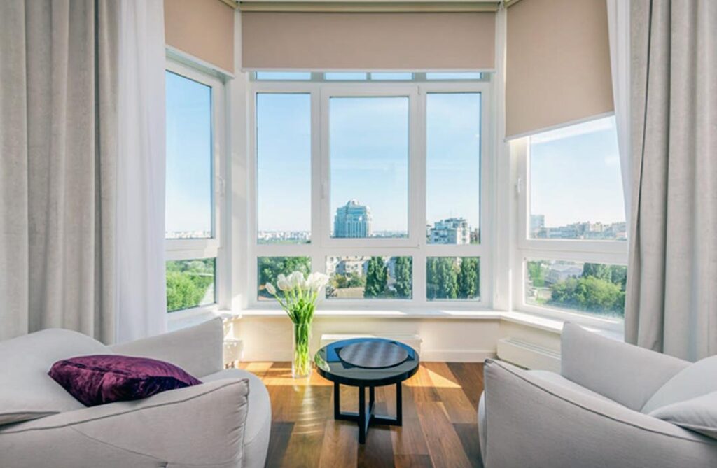 Bright living room with floor-to-ceiling LOW-E windows, providing a clear view of the cityscape while enhancing energy efficiency and natural light, framed by white curtains and minimalist decor.