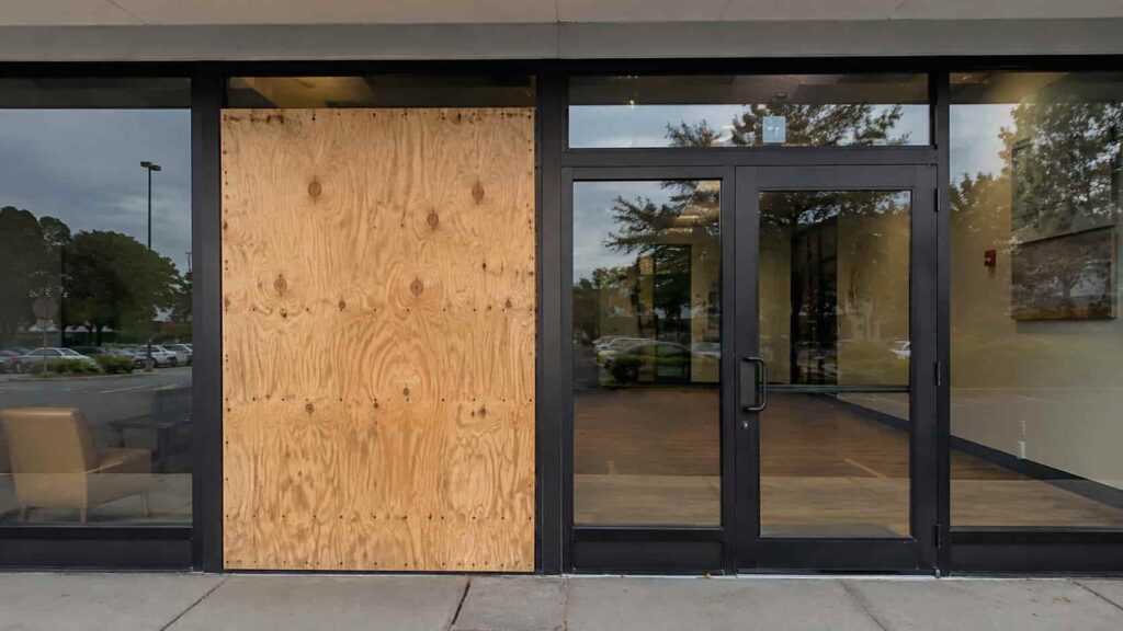 Commercial storefront with one damaged glass opening securely covered by fitted plywood